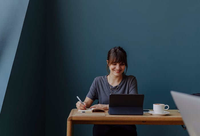 A smiling person at a desk taking notes.