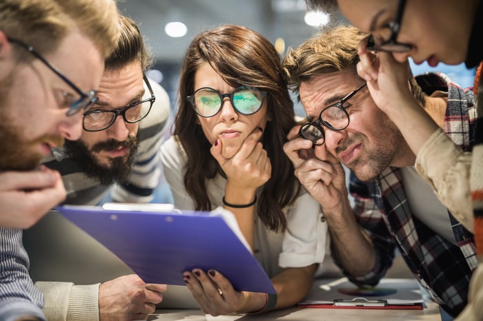 A group of five people looking confused while reading a report.