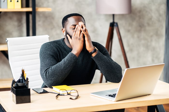 A person at a laptop covering their face.