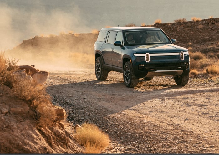 Green Rivian R1S SUV on dirt road.