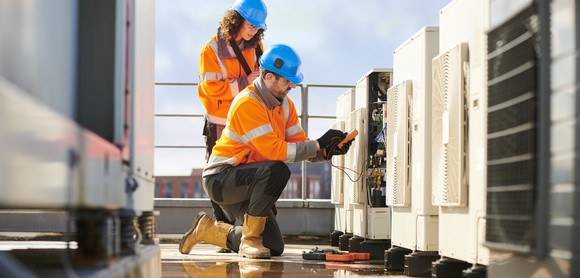 Two workers inspect a rooftop HVAC unit.
