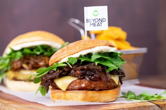 Two Beyond Meat burgers inside buns along with cheese, greens, and onions.