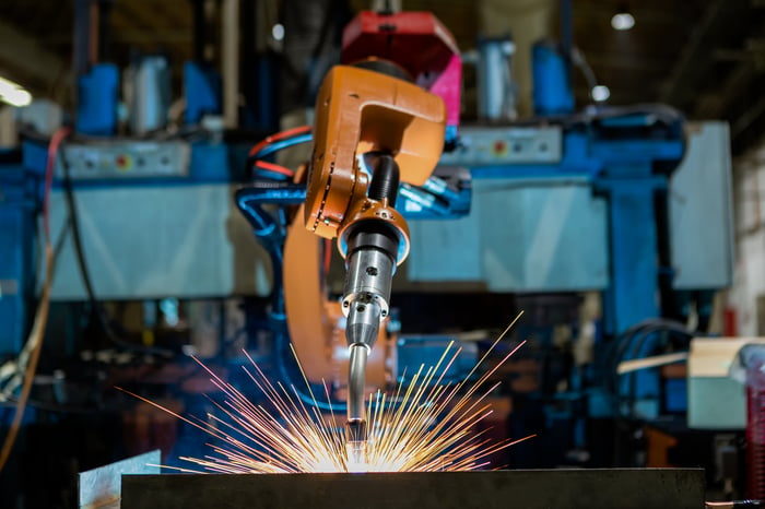 A robotic arm laser welding automotive parts in a factory.