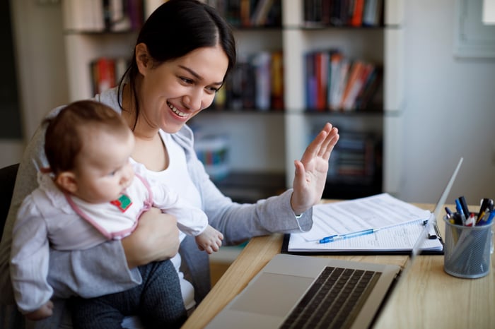 Person holding baby and sitting at desk looking at laptop computer