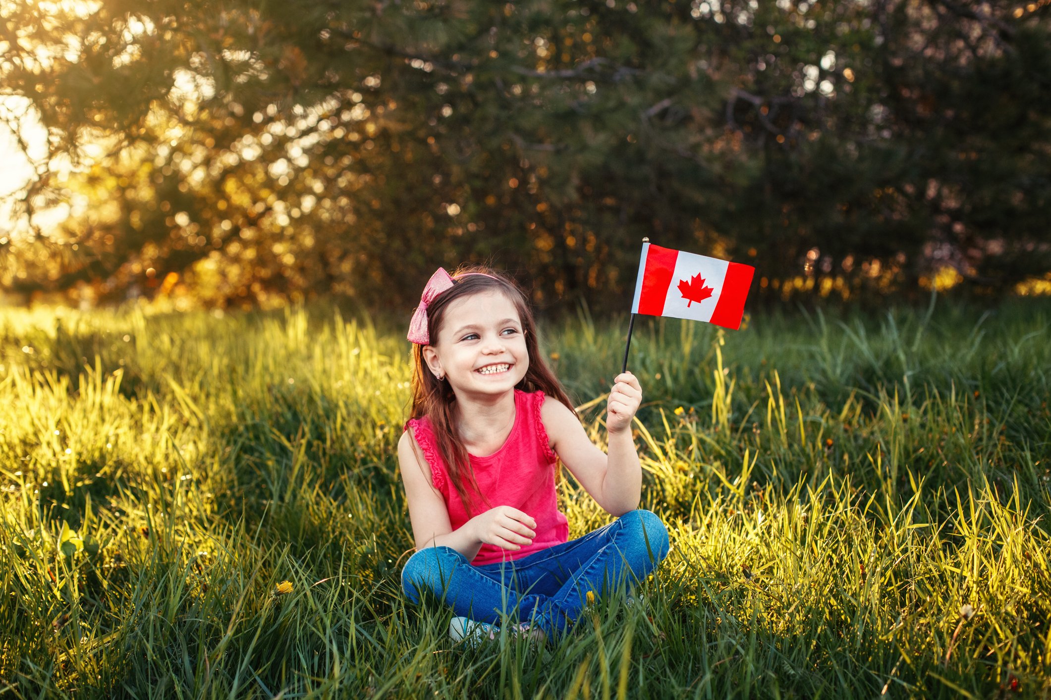 A girl sits in the grass and holds a Canadian flag.