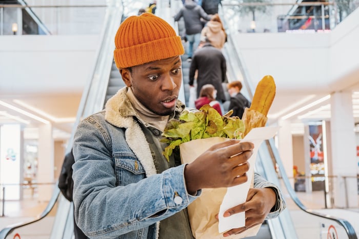 Shopper experiences inflation sticker shock while standing at bottom of escalator. 