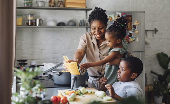 Adult person in a kitchen cooking a meal with two children.