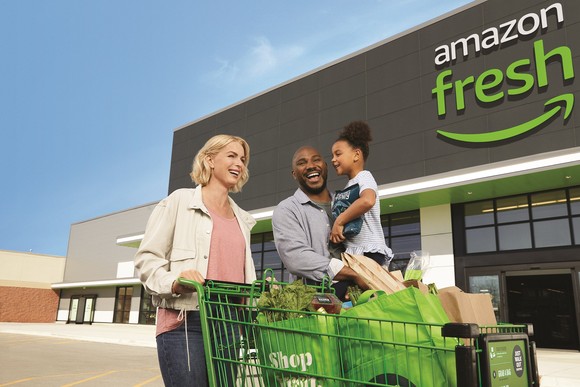 A family outside of an Amazon Fresh store with a wagon and groceries.