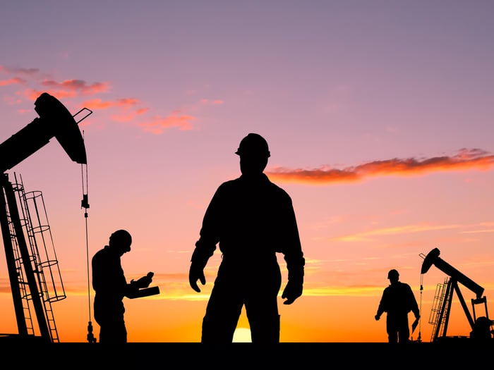 Three people in silhouette with oil rigs in the background.