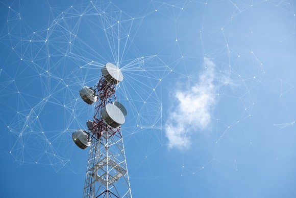 Cell tower against a bright blue sky with white lines representing a computerized cell network.