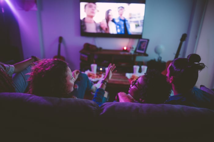 Three young people seated on a couch and watching TV.