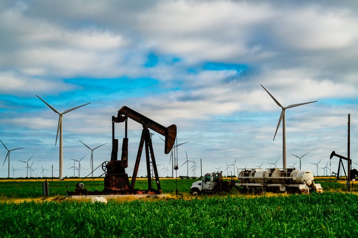 An oil well with wind turbines in the background.