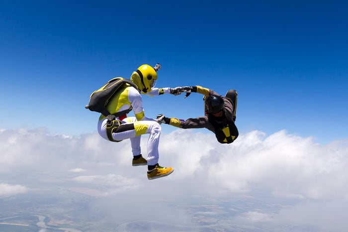 Two people holding hands while skydiving against the bright blue sky backdrop.