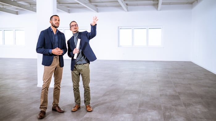 Two people standing in a large empty room.