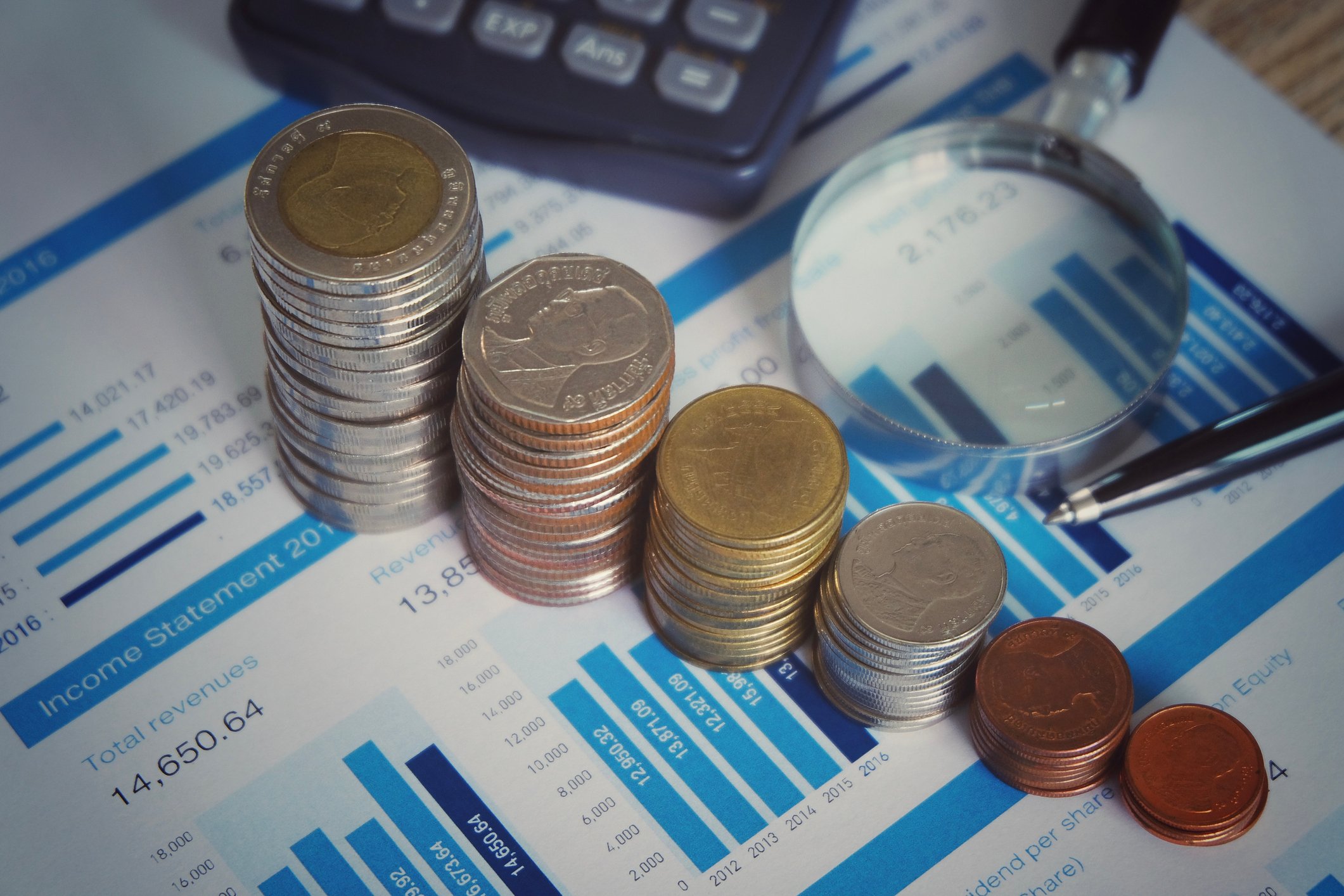 Coins stacking and chart with magnifying glass for analyzing financial report