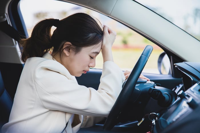 Japanese driver leans against car steering wheel and looks upset.