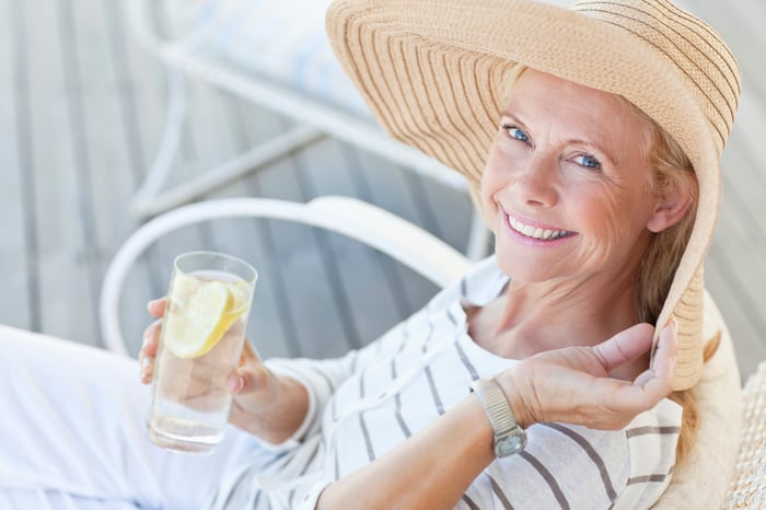 A woman wearing a large floppy hat and holding a glass with lemons and water.