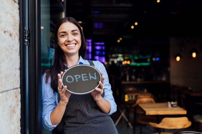 A restaurant worker holding a sign that says 'Open.' 