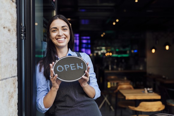 A restaurant worker holding a sign that says 'Open.'