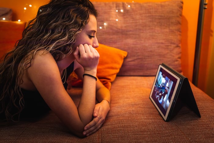 Girl watching streaming TV on a tablet while lying on a couch.