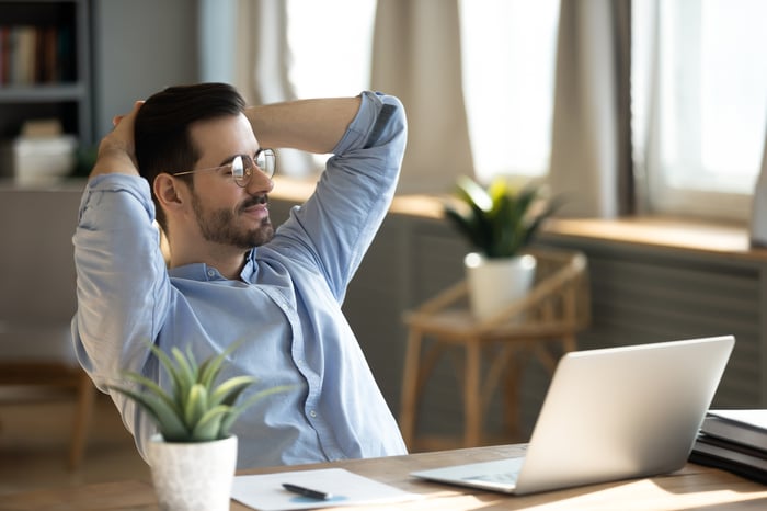 A person with hands behind head looking at a laptop.