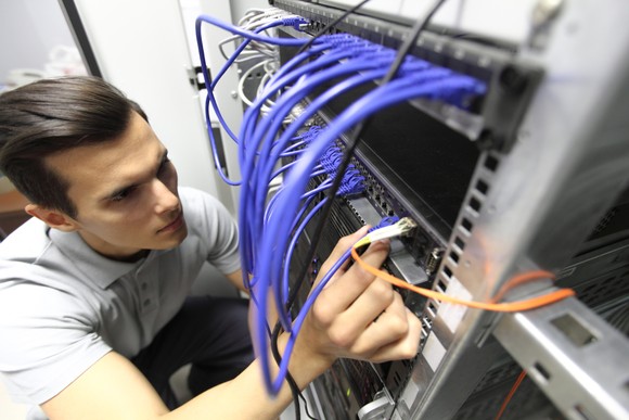 An engineer plugging cables into the back of a data center server tower.