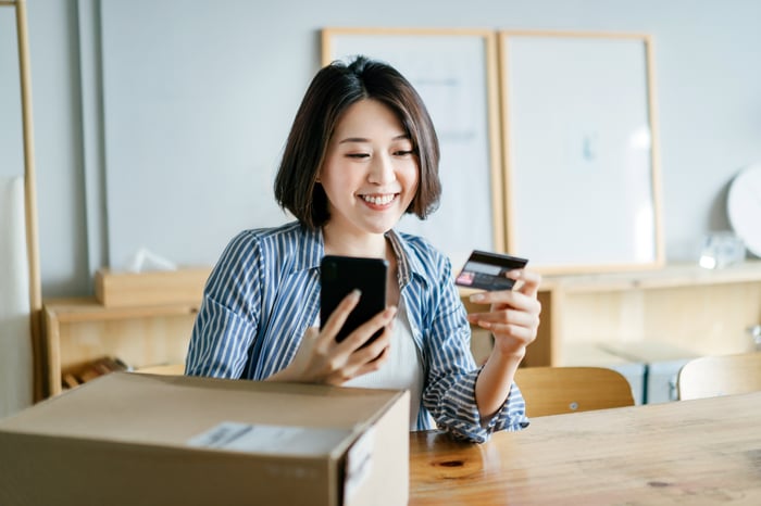 Person entering credit card info into a smartphone with a package sitting nearby.