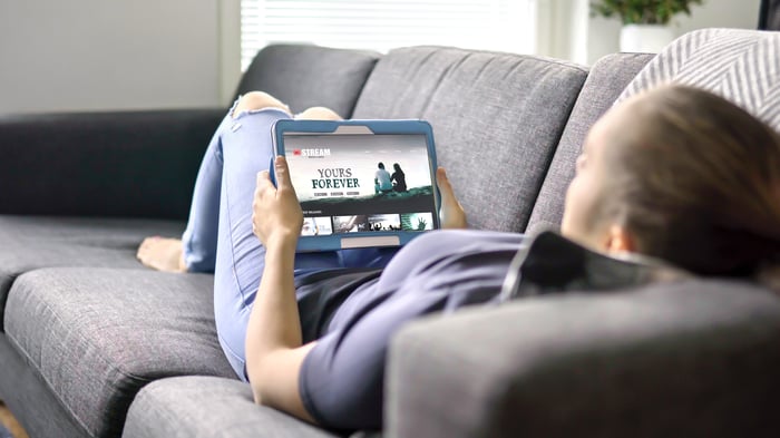 A person lies on the couch watching a video on a tablet.
