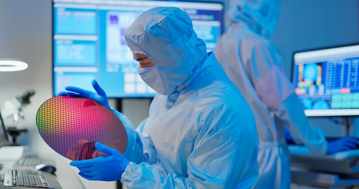 Worker in a clean room suit examines a silicon semiconductor wafer.