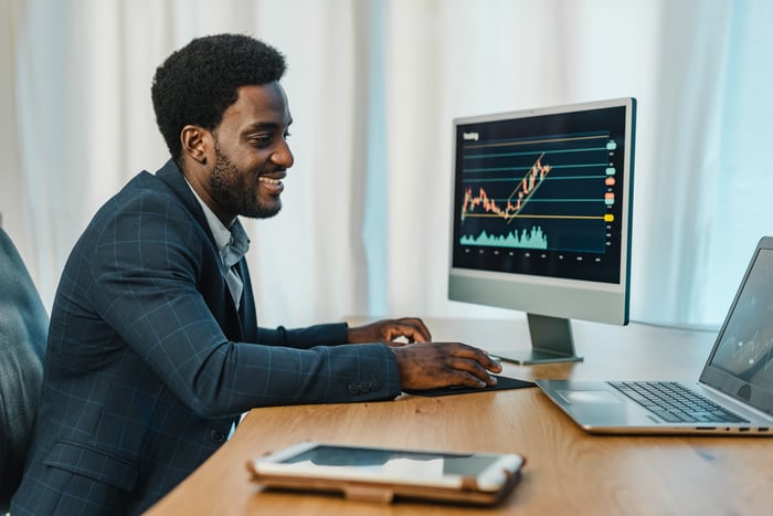 A person in a formal suit looking at stock price charts on computer screens.