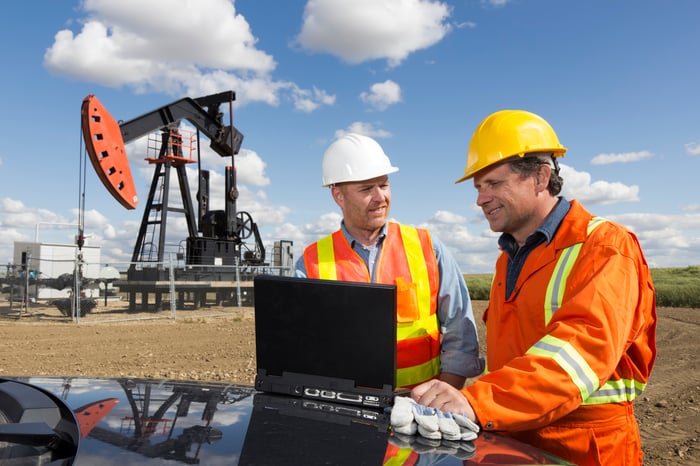 Two oil workers using a laptop in front of an oil rig.