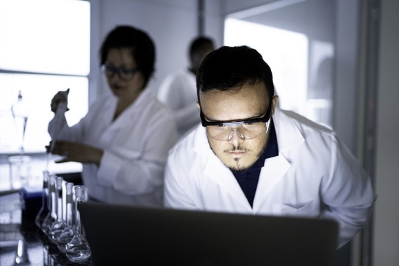 A scientist studies something on a laptop in a lab.
