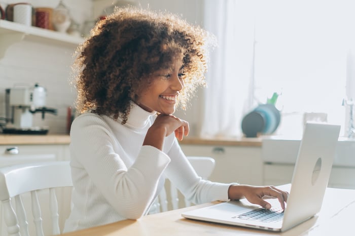 A person sitting at their desk smiling at their laptop computer.