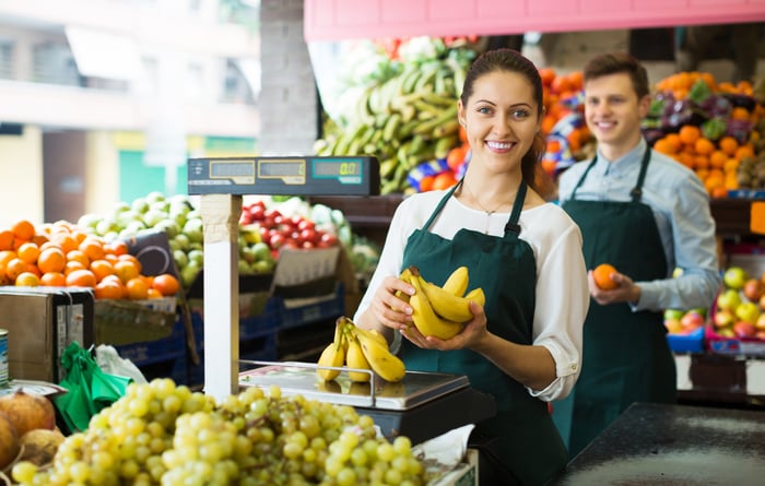 An employee in a grocery store holding fruit in the produce department.