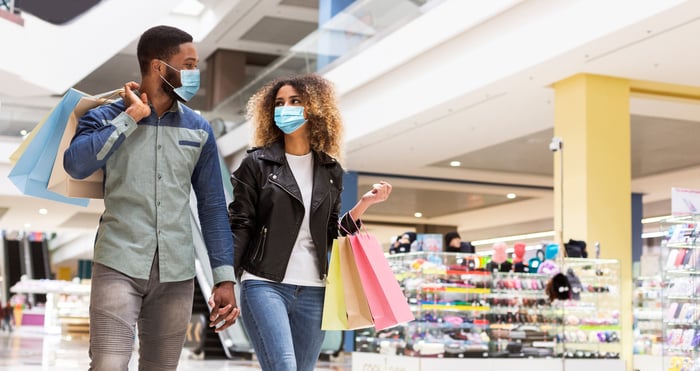 Two masked people in a store holding hands and carrying shopping bags.