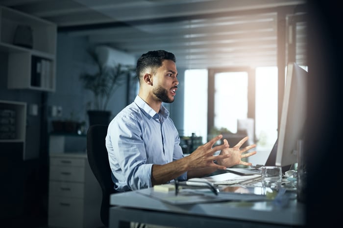 An angry person with hands outstretched looking at a computer monitor.