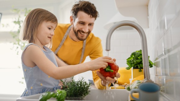 An adult and a child washing vegetables at a kitchen sink.