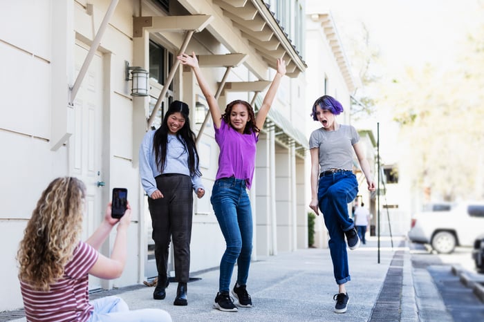 A young person filming a group of friends with a smartphone. 