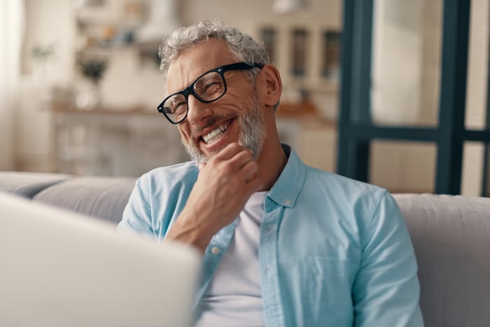 A smiling person sitting with a laptop.