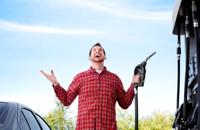 Person looks to sky while holding a gas pump handle at a gas station.