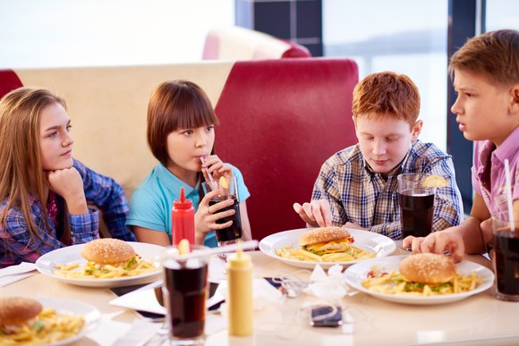 A group of kids eating burgers and fries and drinking soda.