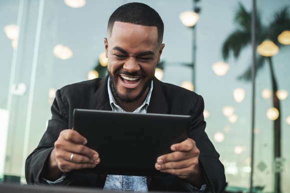 A person smiles at a tablet while sitting outside.