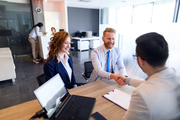Professionals are shaking hands at a desk in an office setting.