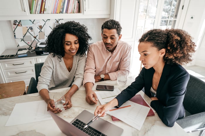 Three investors sit around a desk and look at something on a laptop.