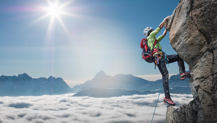 A climber clinging to rocks near mountain summit.