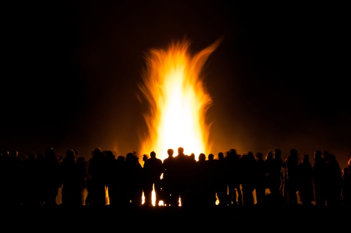 Crowd of people gathered around a bonfire at night.
