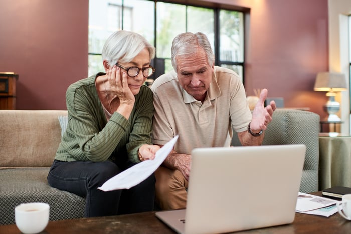 Two people sitting on a couch looking at a laptop.