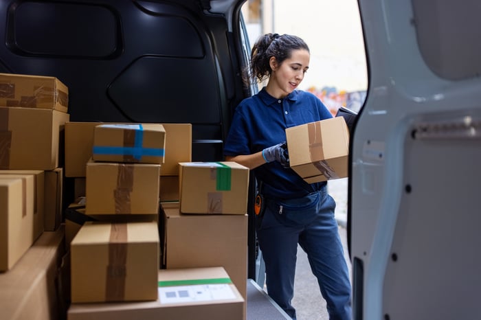 A person with a package next to a van with boxes.