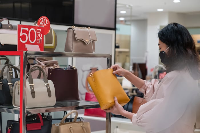 Masked shopper looking at pocketbooks marked 50% off.