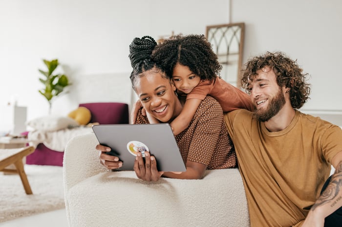 Two adults and a child smile while watching content on a tablet.